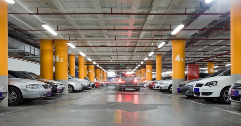 A view down a long aisle of an underground parking garage with rows of parked cars and bright yellow support pillars.