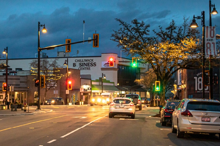 downtown Chilliwack street in the evening showing a shite car in a right turn lane with a green light above.