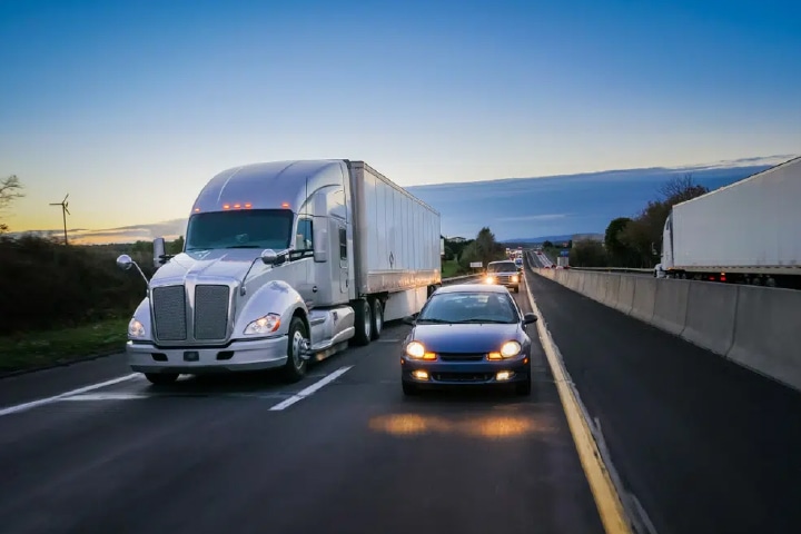 a two lane road with a car driving beside a white semi truck.