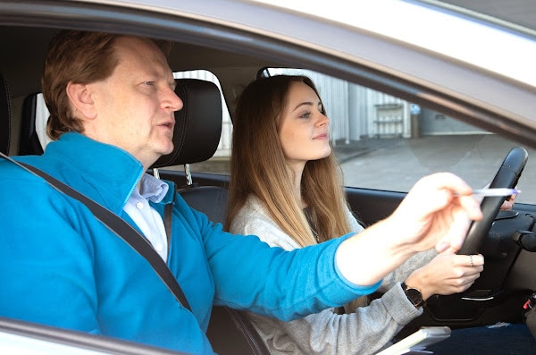 Male Driving Instructor giving direction to young woman who is driving.