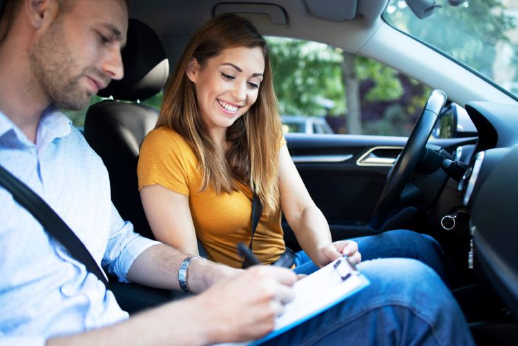 a man holding a clipboard in the passenger seat of a car is showing the clipboard to the young woman in the driver's seat.