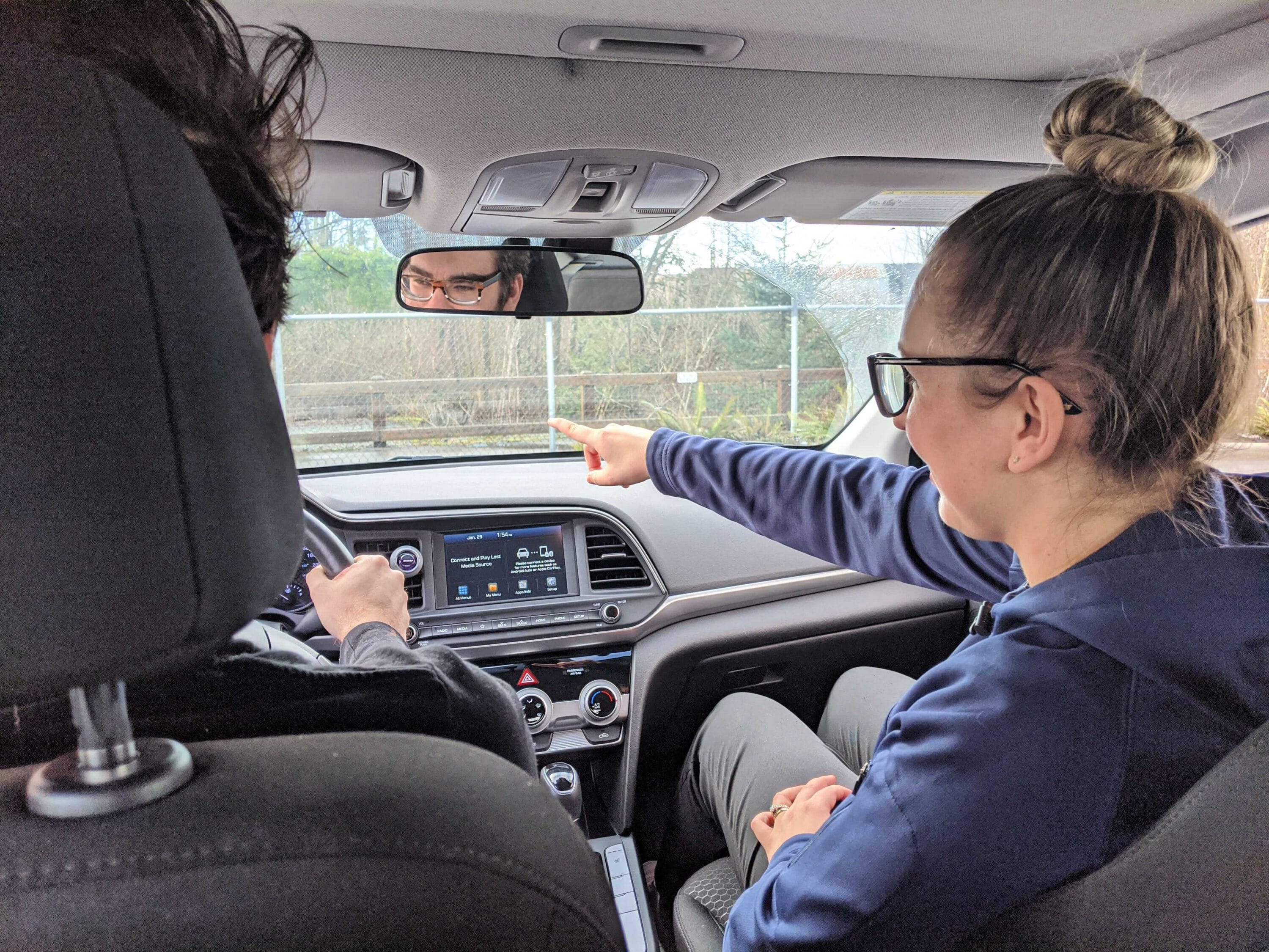 view from the back seat of a car.  a woman in the passenger seat is giving directions to the driver.