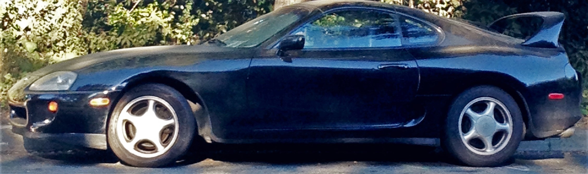 A side profile of a dark blue Toyota Supra MK IV parked on an asphalt surface.