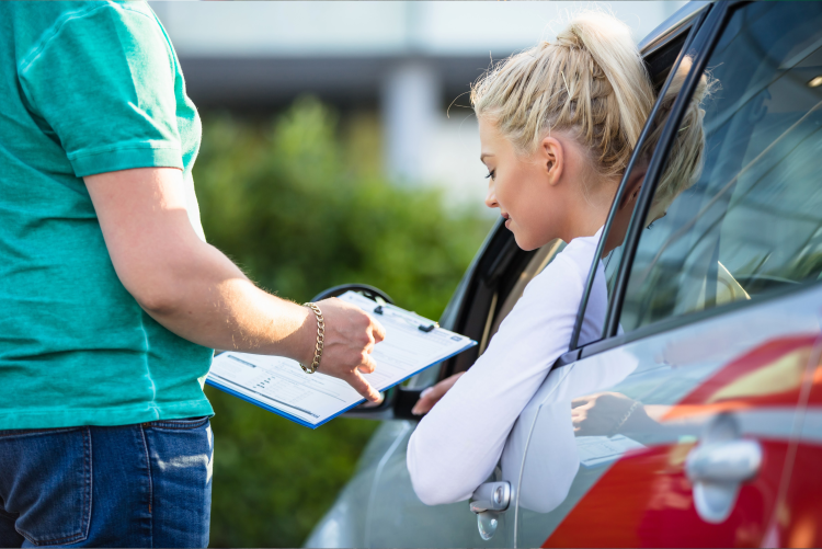 a young female driver leaning out of the window, talking to a man that is pointing to his clipboard