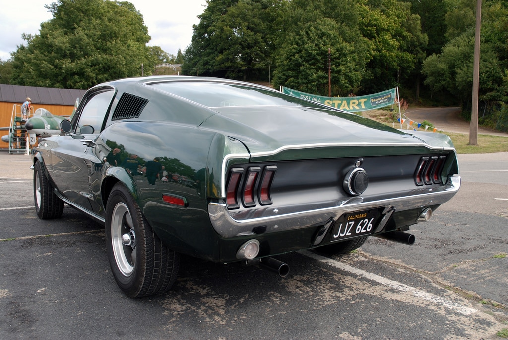 A rear three-quarter view of a forest green 1968 Ford Mustang GT 390 Fastback parked on an asphalt road.