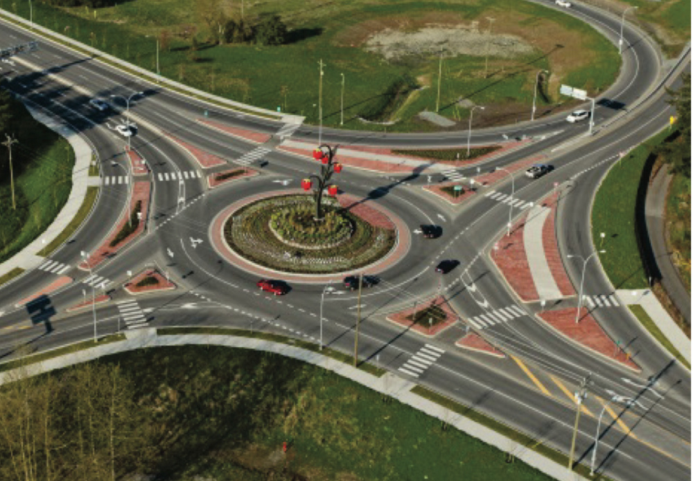 Multi lane roundabout in Abbotsford with cars driving.  There is a raspberry statue in the grassy area in the middle of the roundabout.