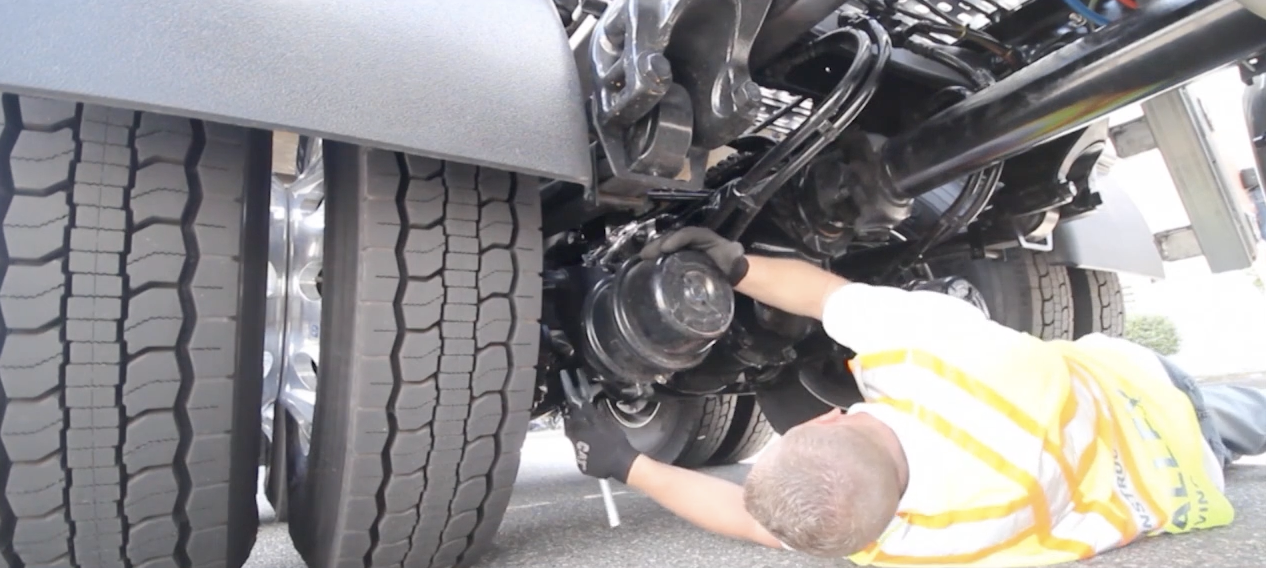 A commercial driver performing a pre-trip inspection and checking the air brake system on a large vehicle, a critical skill for obtaining a commercial license.