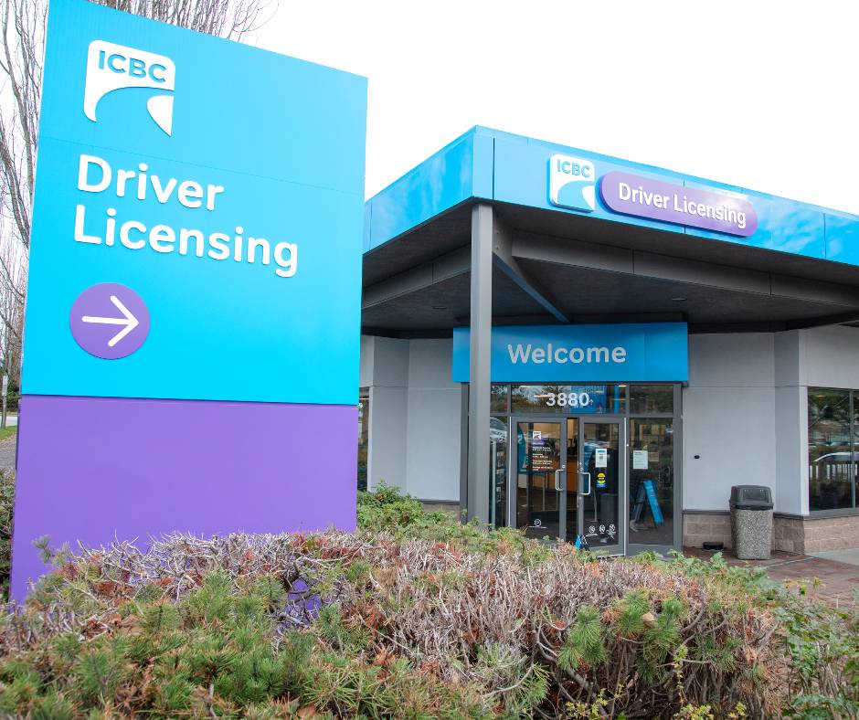 A street-level view of an ICBC Driver Licensing office, featuring a large blue and purple pylon sign in the foreground and a "Welcome" sign above the main glass entrance doors in the background.