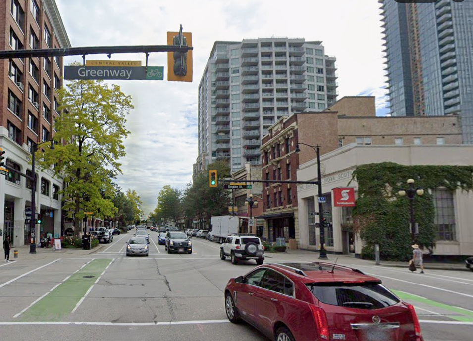 New Westminster Intersection showing a red car driving forward. There are high rise buildings in the distance.