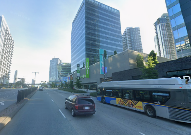 Multilane road in Surrey with a maroon mini van and transit bus travelling down the road. there are high rise buildings on either side of the road.