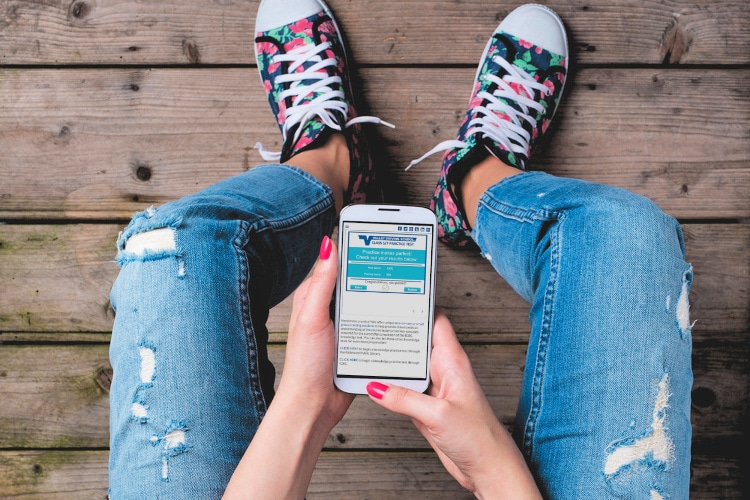 a young person wearing distressed jeans is holding a phone to answer test questions.