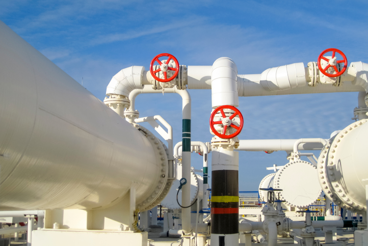 A complex network of large white industrial pipes and tanks featuring several prominent bright red valve wheels, set against a clear blue sky.