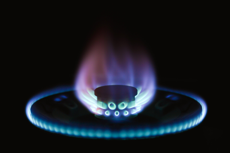 A lit gas burner showing a circular ring of glowing blue flames and a central flame with purple and red tints, isolated against a solid black background.