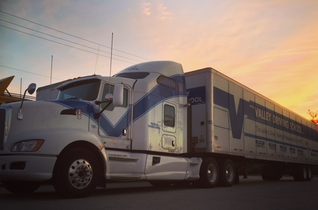 a white semi truck with a blue stripe on it, parked at sunset.
