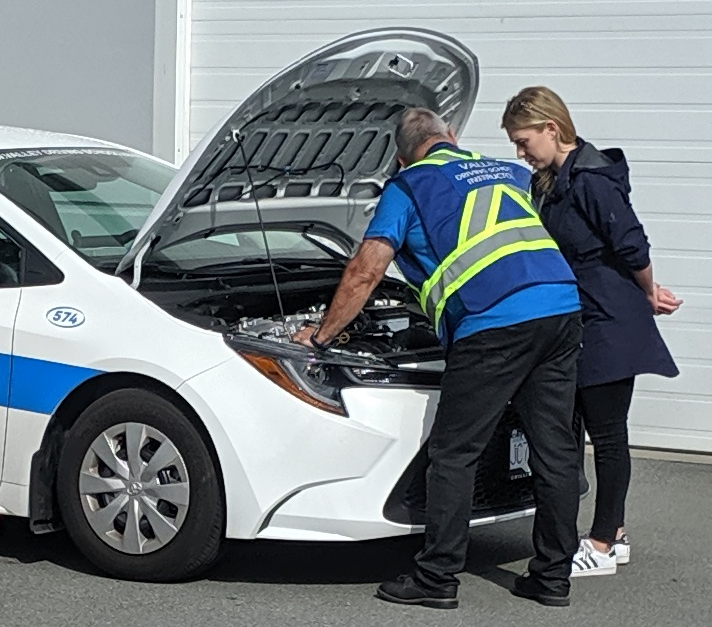 A Valley Driving School Instructor in a safety vest showing a student driver how to perform a class 4 pre-trip inspection.