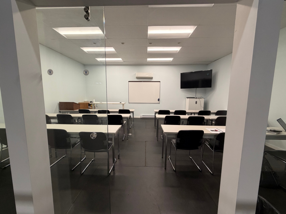 A classroom with tables and chairs. A blank white board and TV are at the front of the classroom.