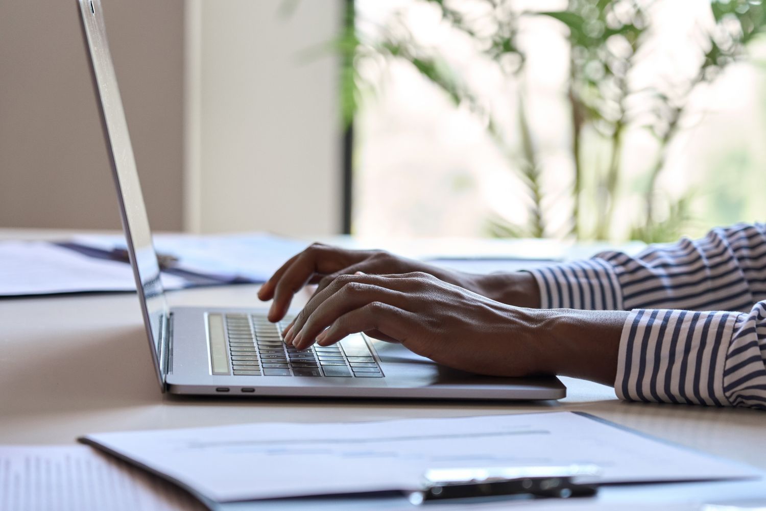 A person using a laptop computer at a desk with a pair of eyeglasses resting nearby.