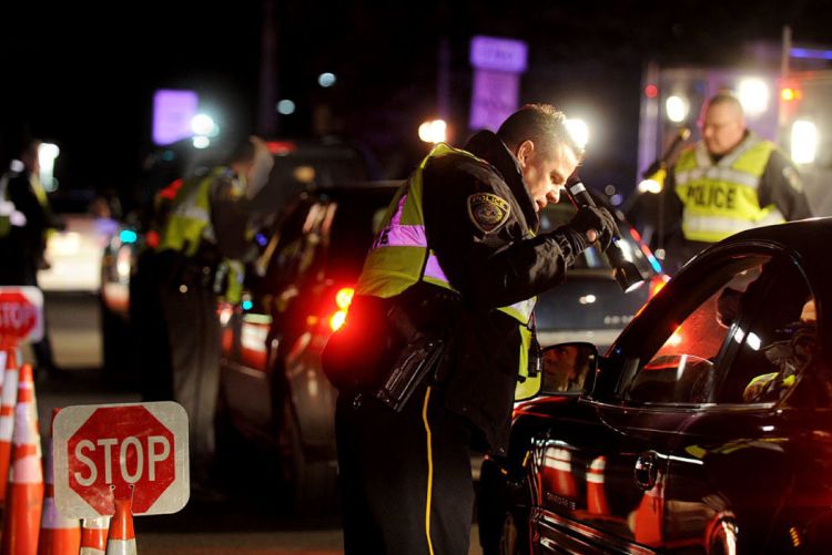 A police officer shining a flashlight into a vehicle at night during a police checkpoint roadblock.