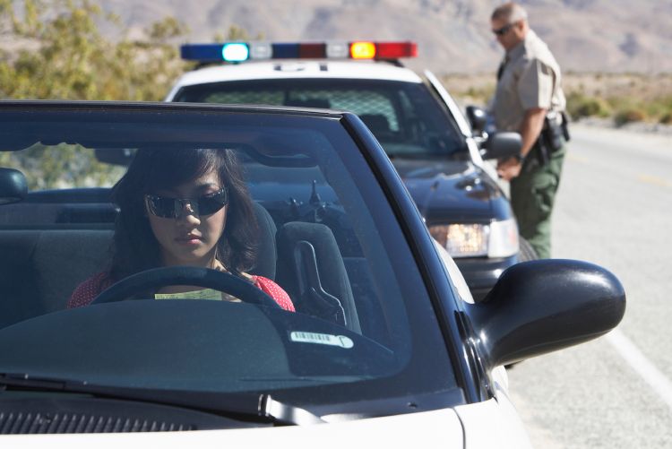 A view from the front of a car, of a police cruiser pulled over on the side of a road with its flashing blue and red emergency lights activated.