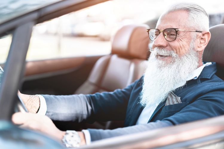An older adult man smiling while driving a car.