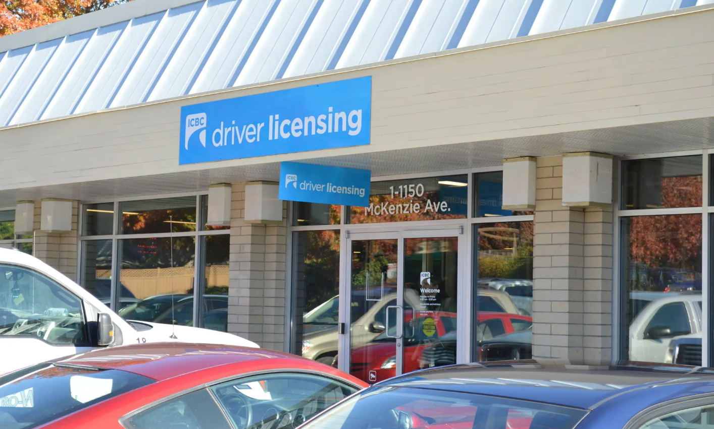 An exterior view of a ICBC driver licensing office with various cars parked in front and a clear blue sky above.