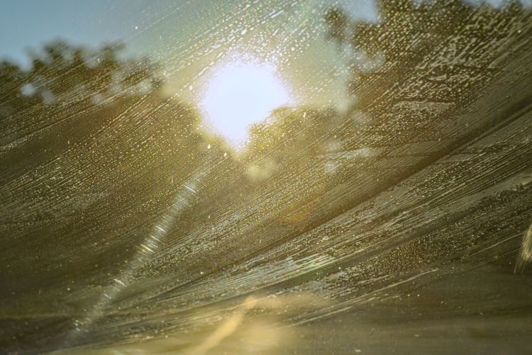 A view through a dirty car windshield with a visible crack, with bright sunlight creating significant glare across the glass.