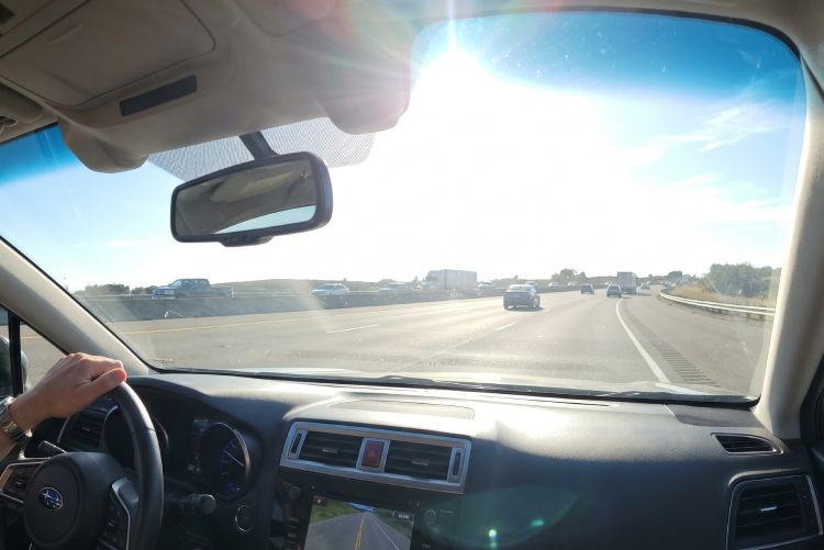 A car driving on a three-lane freeway as blinding sun glare comes through the windshield