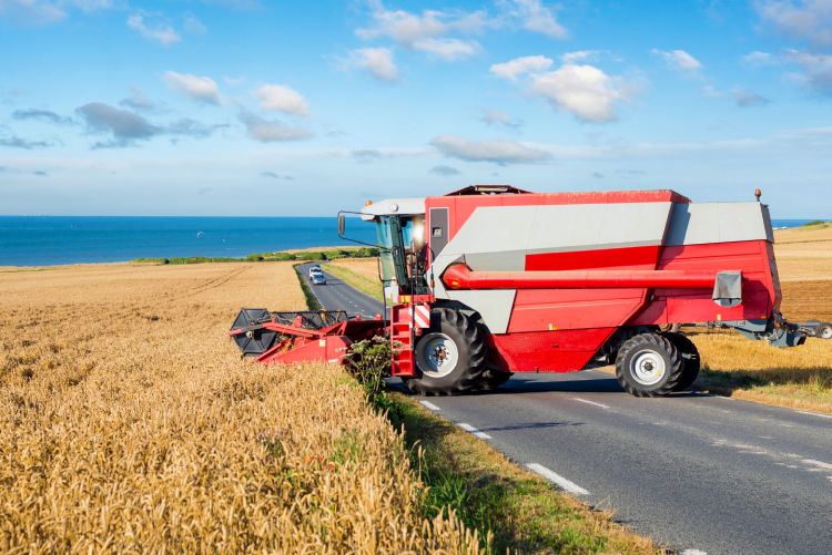 A large red and white combine harvester machine working in an open agricultural field under a clear blue sky.
