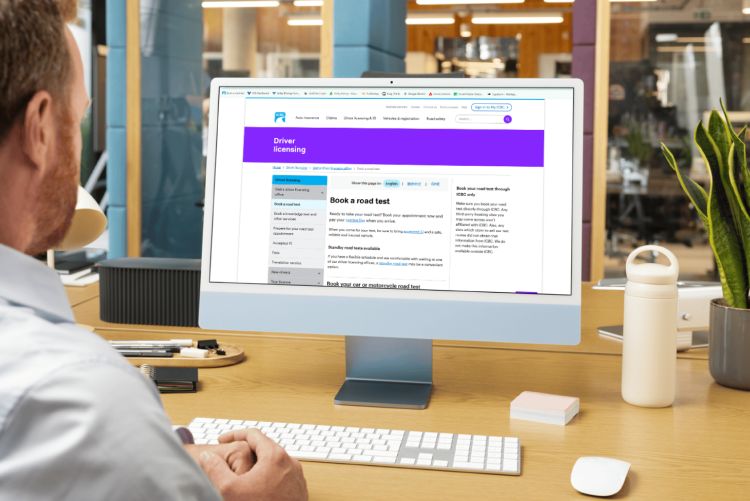 A man sitting in front of a computer sitting on a desk, displaying ICBC's road test booking webpage.