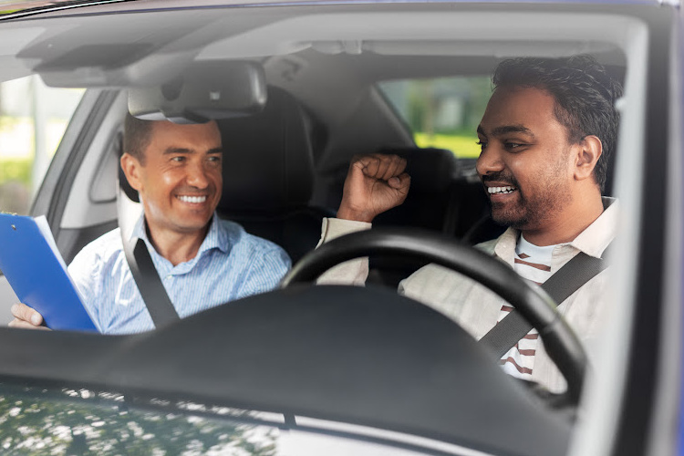 This image shows a happy driving instructor in the passenger seat and cheering student driver, debriefing after a lesson.