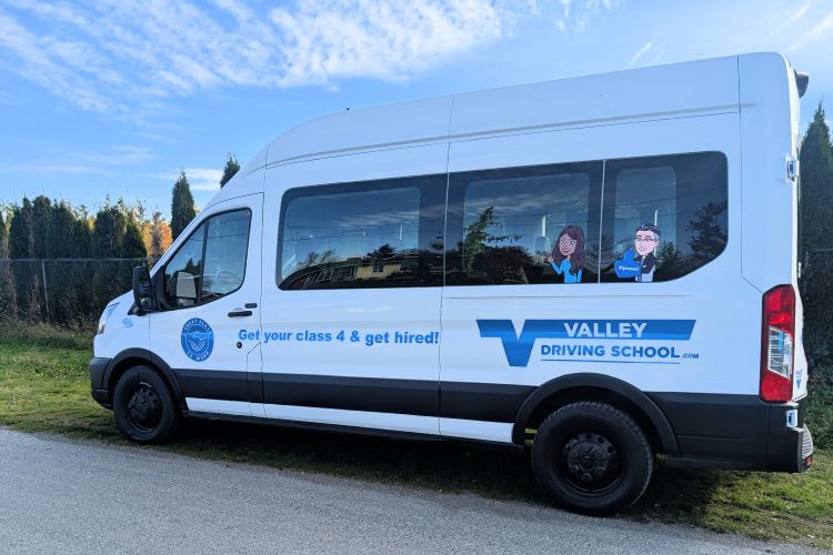 A photo of a white transit van driving on a residential street, with a Valley Driving School decal displayed on the side of the vehicle.