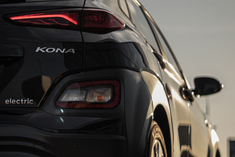 This image is a close-up photo of the rear hatchback and bumper of a modern grey car (specifically a Hyundai Kona Electric), highlighting the vehicle's unique rear taillights and "KONA" emblem.