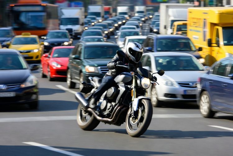 A view of a motorcyclist riding down a busy multi-lane road surrounded by dense car traffic on both sides.