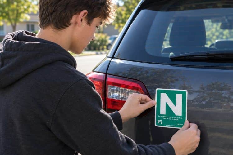 A driver adjusting a green "N" sign displayed on the back of a car.
